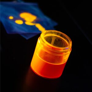 Photo of a quantum dot ink solution emitting an orange glow under ultraviolet excitation.